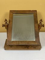 Front view of the antique wooden shaving mirror showing the rectangular mirror with turned wooden side supports and knobs.