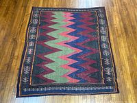 Full view of rectangular area rug with zigzag design and geometric patterned borders on wooden floor.