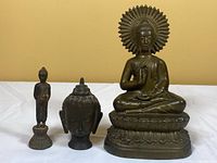 Three bronze Buddha figures side by side on white cloth