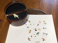 Overview of cuff links on white surface with open Bombay style wooden storage box featuring black fabric interior.