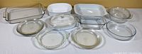Overview of all glass and ceramic bakeware items on a beige background, showing clean surfaces and multiple dish shapes and sizes