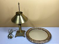 Brass footed lamp and round mirror on table against wall, showing overall condition and size.
