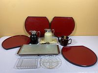 Overview of lot showing four red lacquered trays, enamel tea pot, two metal coffee pots, electric cook top, and glass dishes.
