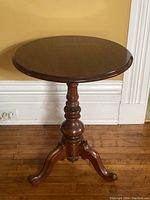 Side view of the wooden pedestal table showing the round top, turned central column, and tripod curved legs.