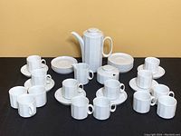 Full demi-tasse set laid out with all cups and saucers, tall pot, creamer, and sugar holder visible on black surface.