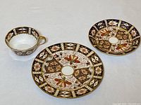 Tea cup, saucer, and small side plate laid out separately showing detailed pattern and gold trim.