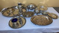 Wide shot of entire silver plate serving lot on white tablecloth showing all items including trays, pitcher, salt and pepper shakers, covered dish, and small bowl with blue liner.