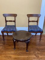 Full view of round wooden table between two wooden chairs with upholstered striped seats on wooden floor