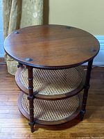 Full view of round mahogany tiered side table with cane woven shelves and carved legs