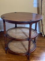 Front view of the round mahogany side table with three tiers and cane webbing shelves.