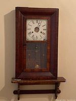Frontal view of vintage New Haven Clock Company wall clock, showing wood frame and closed glass panel, white Roman numeral clock face with wear.
