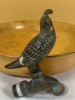 Metal water faucet with bird handle in front of wooden bowl, showing wear and paint chipping on the bird figure.