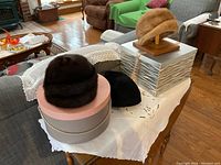 Three hats displayed on two hat boxes and a wooden stand on a crocheted cloth