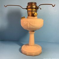 Side view of the Aladdin oil lamp showing pink glass Lincoln Drape design and brass burner with wick knob