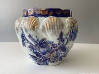 Front view of antique planter showing flow blue floral pattern with gold highlights and raised clamshell shapes on the ceramic surface.