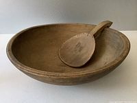Antique wooden dough bowl with wooden butter paddle inside, showing interior and bowl shape
