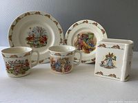 Photo showing full set including two plates, two mugs, and rectangular bank with Bunnykins designs.