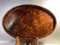 Front view of the oval burled wood tray displayed upright showing the intricate wood grain pattern and glossy finish.