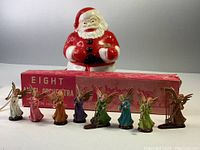 Vintage light-up ceramic Santa figurine and boxed set of eight colorful orchestra angel figurines arranged in front of Santa and the box, showing size and condition of items.