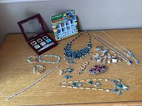 Overview of all costume jewelry items arranged on table including boxed stone charms, necklaces, rings, earrings, and hair clip.