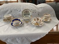 Front view showing all five sets of cups and saucers on white embroidered cloth