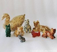 Eight carved stone figures including seven cats and one swan shown on white background, displaying details and size