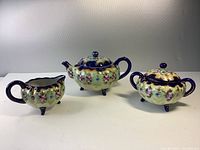 Full view of handpainted tea set with teapot, creamer, and sugar bowl arranged side by side showing floral decorations and cobalt blue accents.