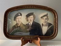Framed photo showing three members of HMCS Canada in uniforms, displayed on a wooden stand, visible frame damage and convex glass.