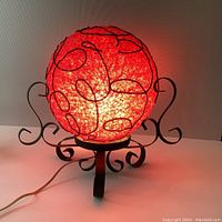 Front view of the illuminated lamp showing glowing red lucite shade with black spiral accents and curled metal base.