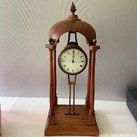 Front view of vintage English mantel clock showing wooden frame with four columns, dome top with finial, round clock face with Roman numerals.