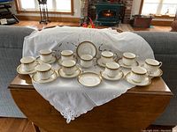 Full display of 11 cups and saucers plus one extra saucer on a wooden table with white cloth background