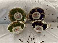 Top view of the two cup and saucer sets showing green and cobalt blue color schemes with floral center designs and gold accents