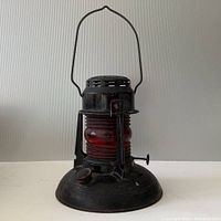 Front view of vintage Dietz No. 40 Traffic Guard lantern showing the red ribbed glass globe and black metal base with handle raised.