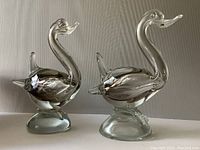 Front view of two handmade clear glass ducks with smoky accents on oval bases