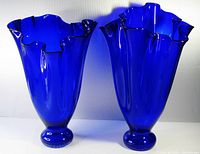 Front and side view of two cobalt blue handkerchief glass vases showing ruffled tops and bases.