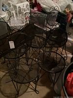 Five black metal bistro chairs grouped together showing mesh seat and back with curved decorative backs.