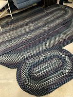 Photo showing two braided rugs with dark blue, burgundy and beige colors with oval shape.