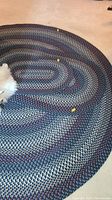 Close-up photo of the large oval braided rug showing multicolored woven pattern in blue, cream, burgundy, and black.
