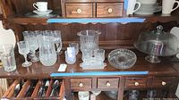 Various French lead crystal barware including wineglasses, pitcher, ice bucket, butter dish, dessert plate, and condiment dish on wooden hutch