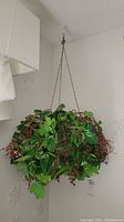 View of a hanging faux plant with green leaves and red berry clusters, attached to the ceiling with chain links.