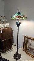 Full view of the floor lamp with stained glass shade illuminated showing height and color.