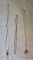 Three necklaces laid out: flat chain with single teardrop pendant, twisted rope chain, station chain with pendants