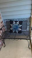 Front view of black metal patio bench with decorative pillow on the seat