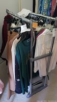 Clothing on adjustable rack showing various sweaters and blouses in different colors including beige, green, white, pink, navy, and black.