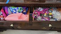 Two drawers shown, left drawer with colorful scarves and pink fabric, right drawer with pink and purple shoelaces and assorted buttons in plastic bags.