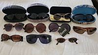 Full lot of ten sunglasses and four cases arranged on a flat surface showing range of styles and designs.