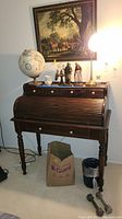 Front view of vintage wooden roll top desk with small drawers and decorative items on top.