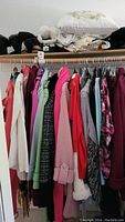 Photo of women's coats and sweaters hanging on rack, showing assortment of colors and styles including white, pink, green, burgundy, and plaid