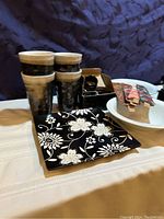 View showing two white ceramic bowls, four tall ceramic cups with brown stripes, black floral plates, and decorative items.