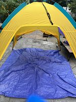 Front view of the yellow and purple pop-up beach tent showing the blue base/floor extended outward on paved ground.
